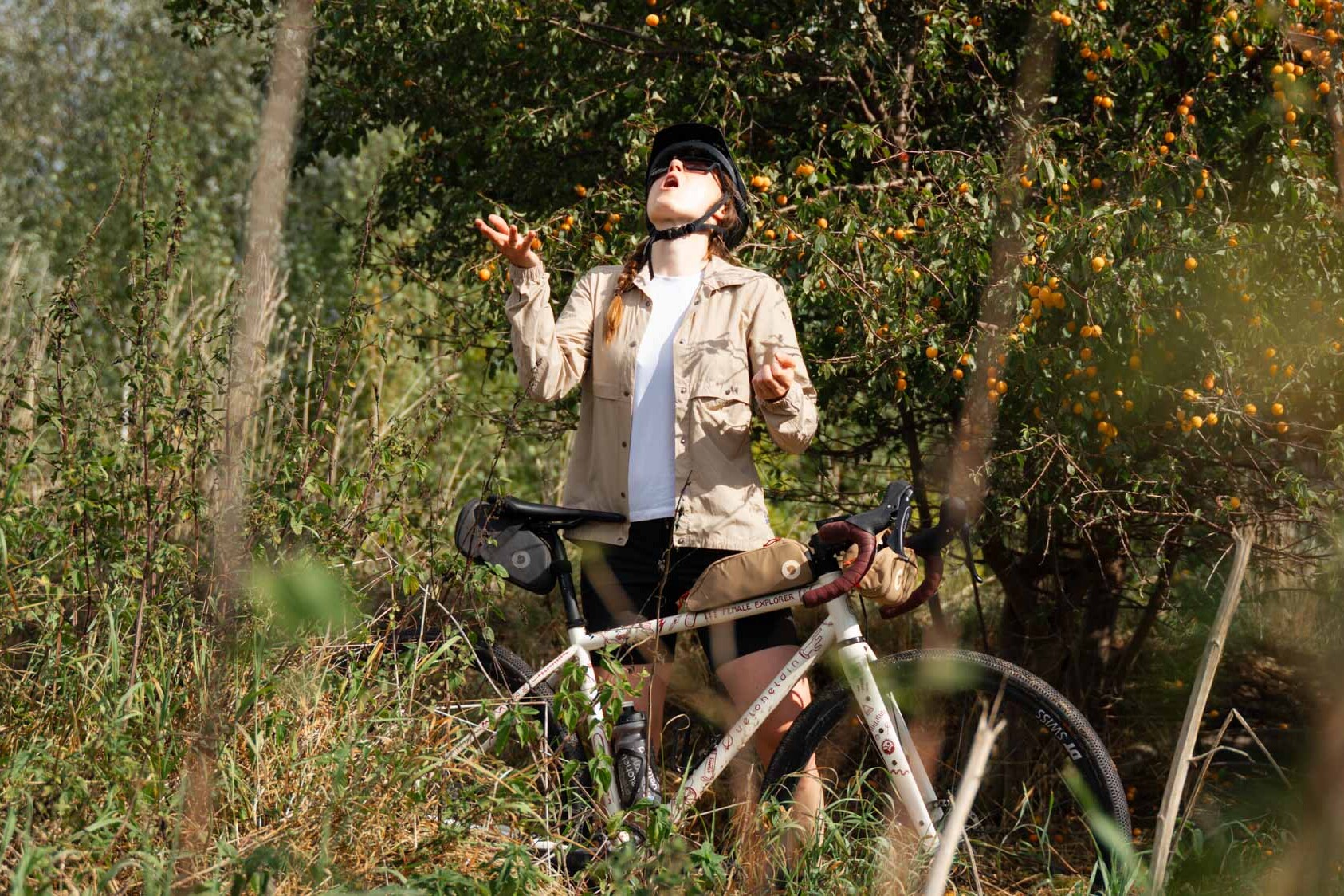 Frau steht vor einem Baum mit Früchten und jongliert mit diesen um sie mit dem Mund aufzufangen, vor ihr steht ein veloheld.iconX