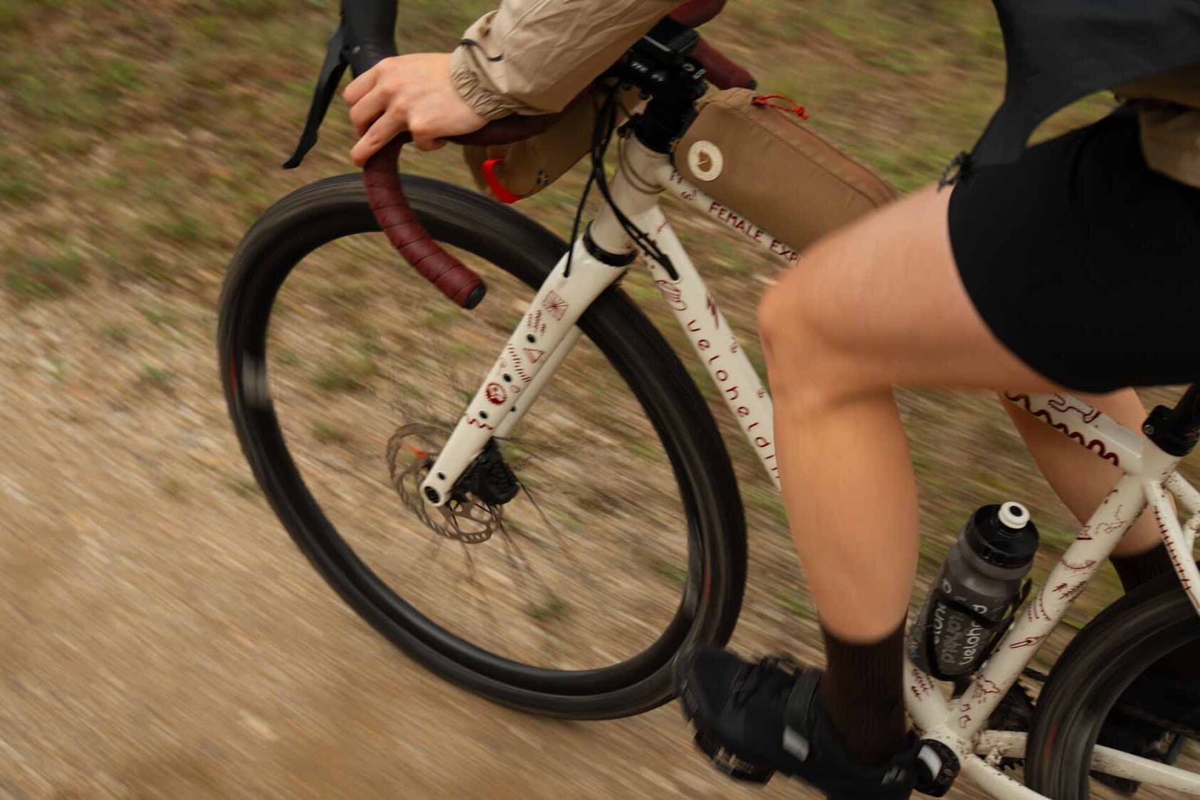 Ausschnitt von einem Gravelbike beim fahren über Schotter, eine Frau sitzt auf dem Gravelbike und am sieht Beine und Hände