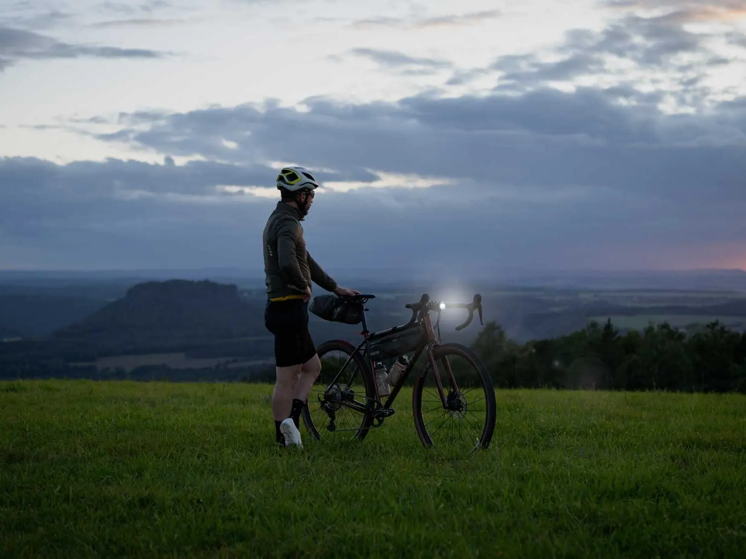 veloheld.iconX Gravelbike auf Wiese im Halbdunkel mit leuchtenden Frontscheinwerfer