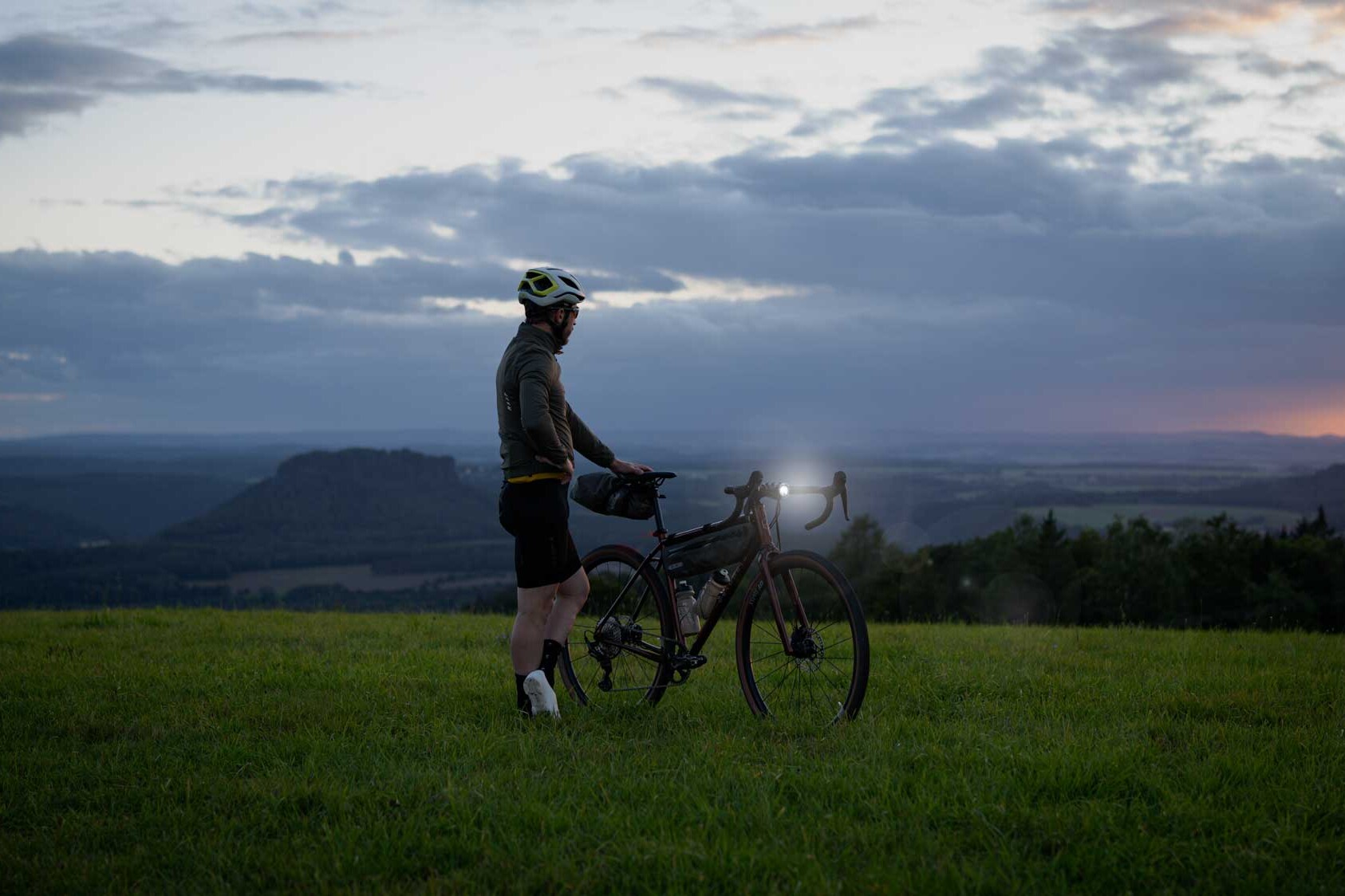 veloheld.iconX Gravelbike auf Wiese im Halbdunkel mit leuchtenden Frontscheinwerfer
