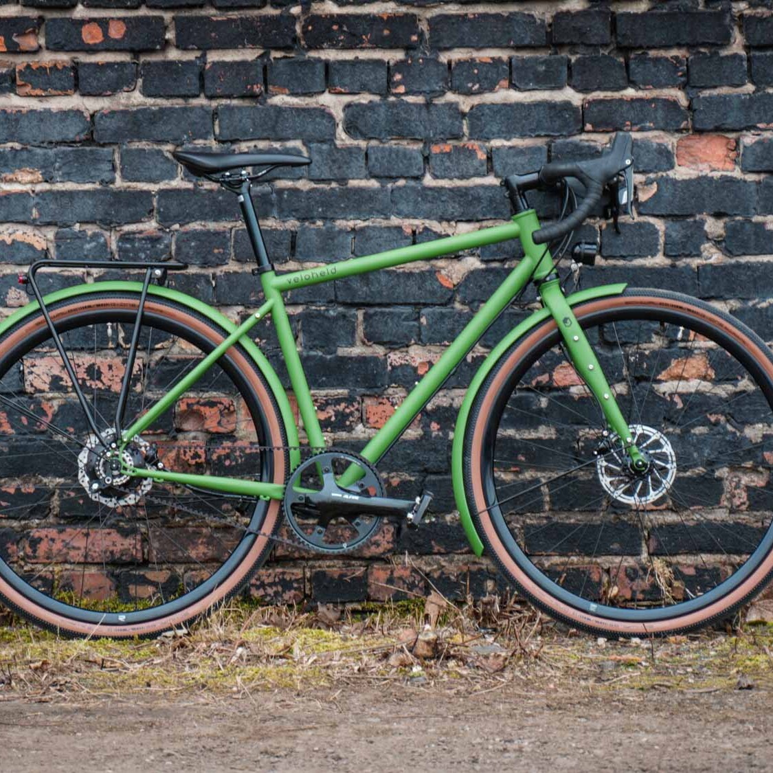 veloheld.alleyX Tourist in grün steht als Komplettrad für einer Steinmauer draußen
