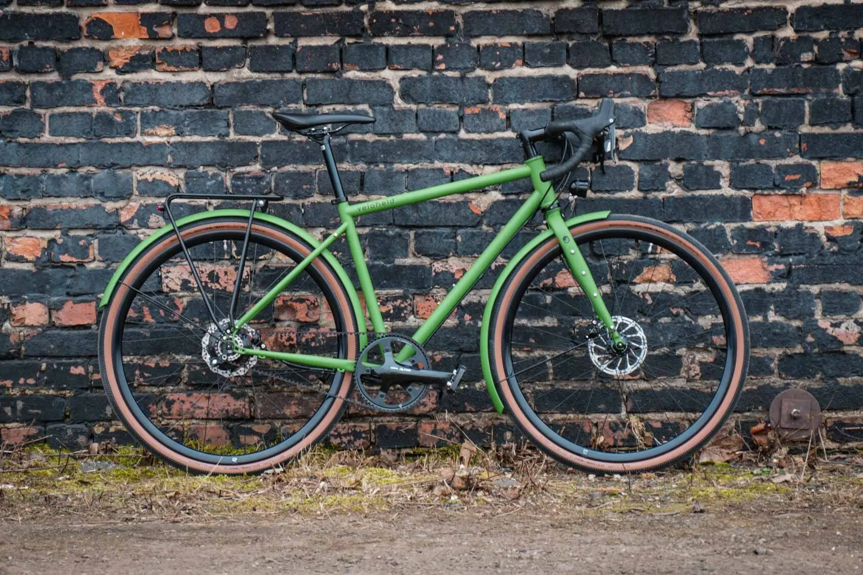 veloheld.alleyX Tourist in grün steht als Komplettrad für einer Steinmauer draußen