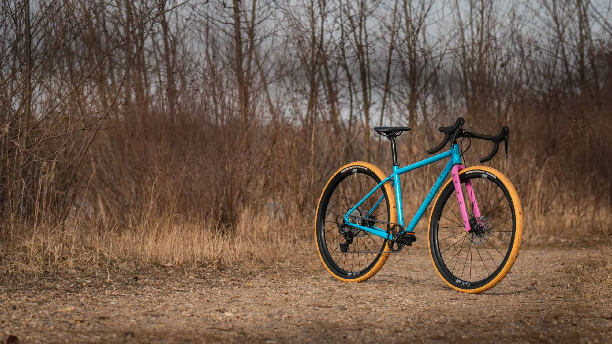 veloheld iconX Custom Gravelbike Bubblegum Farbdesign Detail mit blauem Rahmen und pinker Gabel und gelben Reifen - Komplettrad auf Schotter stehend