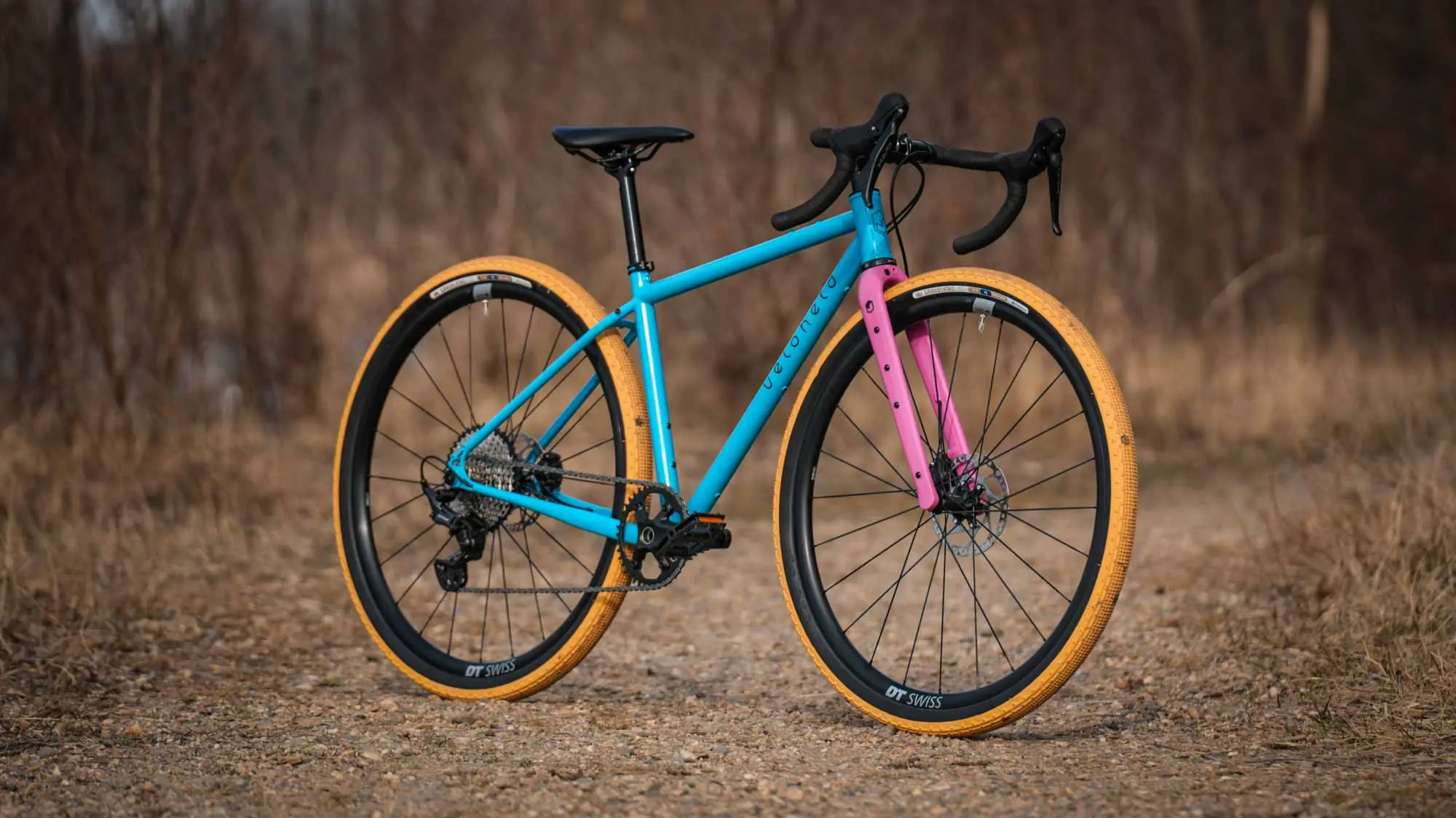 veloheld iconX Custom Gravelbike Bubblegum Farbdesign Detail mit blauem Rahmen und pinker Gabel und gelben Reifen - Komplettrad auf Schotter stehend