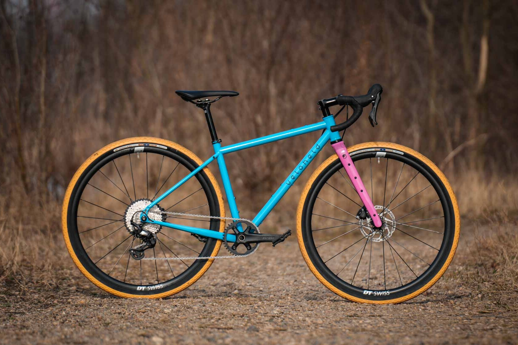 veloheld iconX Custom Gravelbike Bubblegum Farbdesign Detail mit blauem Rahmen und pinker Gabel und gelben Reifen - Komplettrad auf Schotter stehend