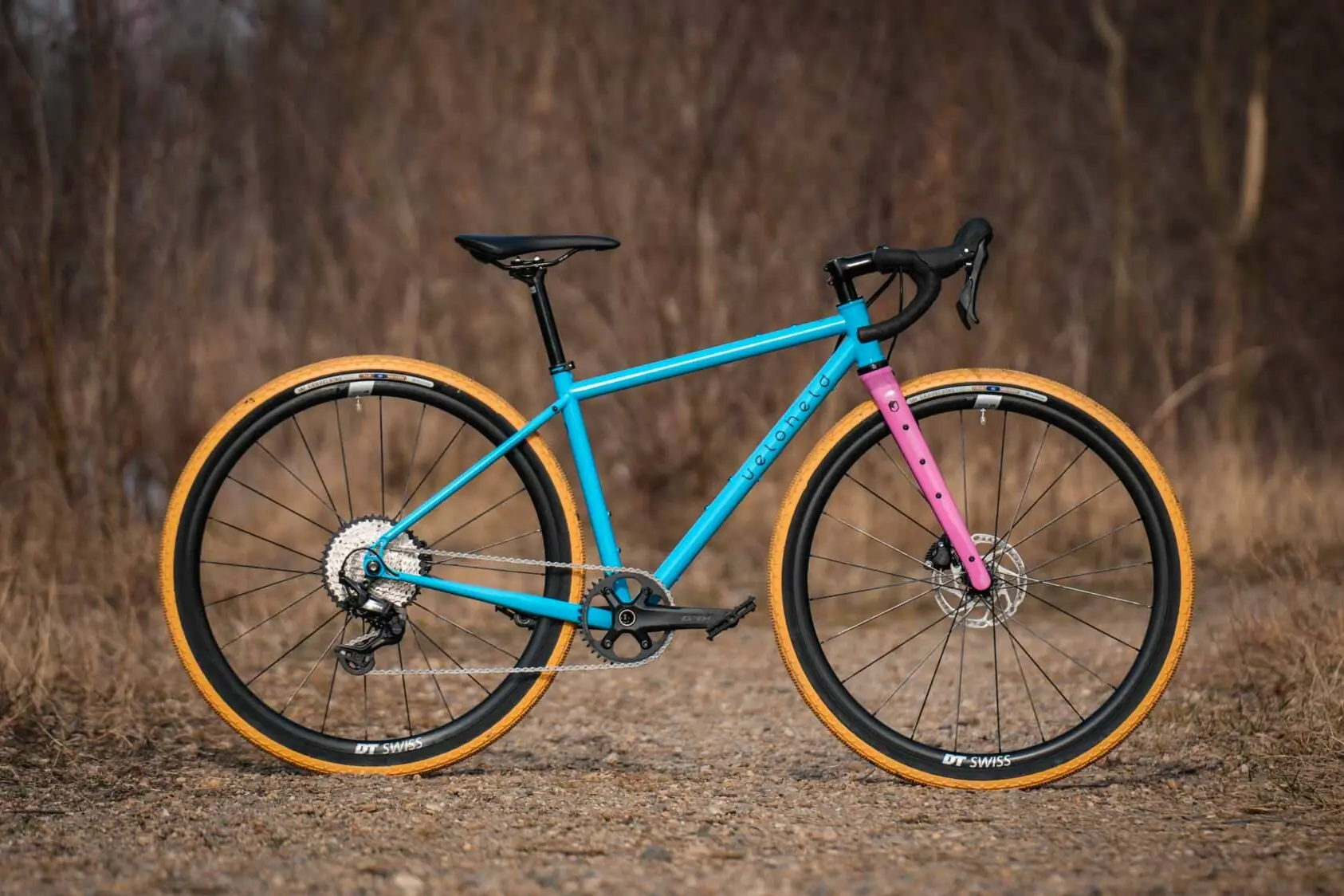 veloheld iconX Custom Gravelbike Bubblegum Farbdesign Detail mit blauem Rahmen und pinker Gabel und gelben Reifen - Komplettrad auf Schotter stehend
