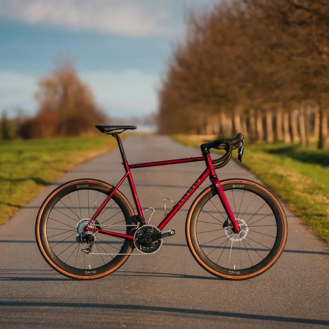 Rotes veloheld.icon Gravelbike mit SRAM Force auf ländlichem Weg in natürlicher Outdoor-Kulisse.