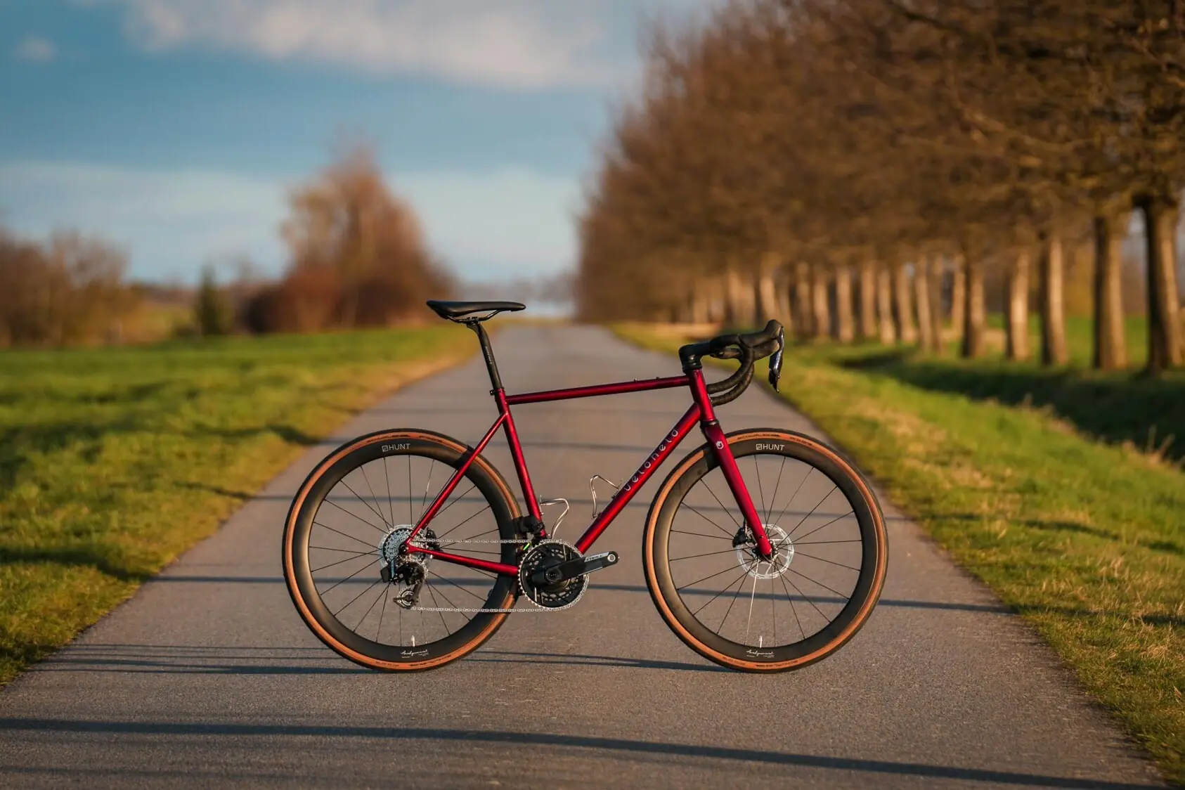 Rotes veloheld.icon Gravelbike mit SRAM Force auf ländlichem Weg in natürlicher Outdoor-Kulisse.