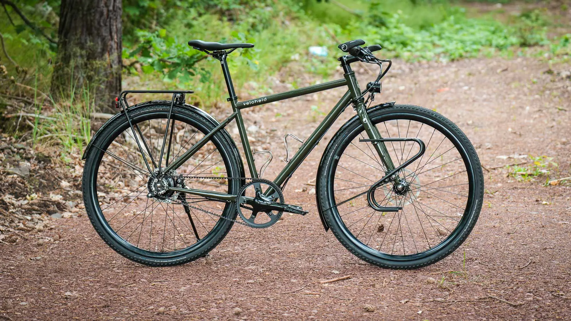 veloheld.alleyX Komplettrad mit Rohloff-Nabenschaltung, Schutzblechen und Gepäckträger als Komplettansicht auf einem Waldweg.